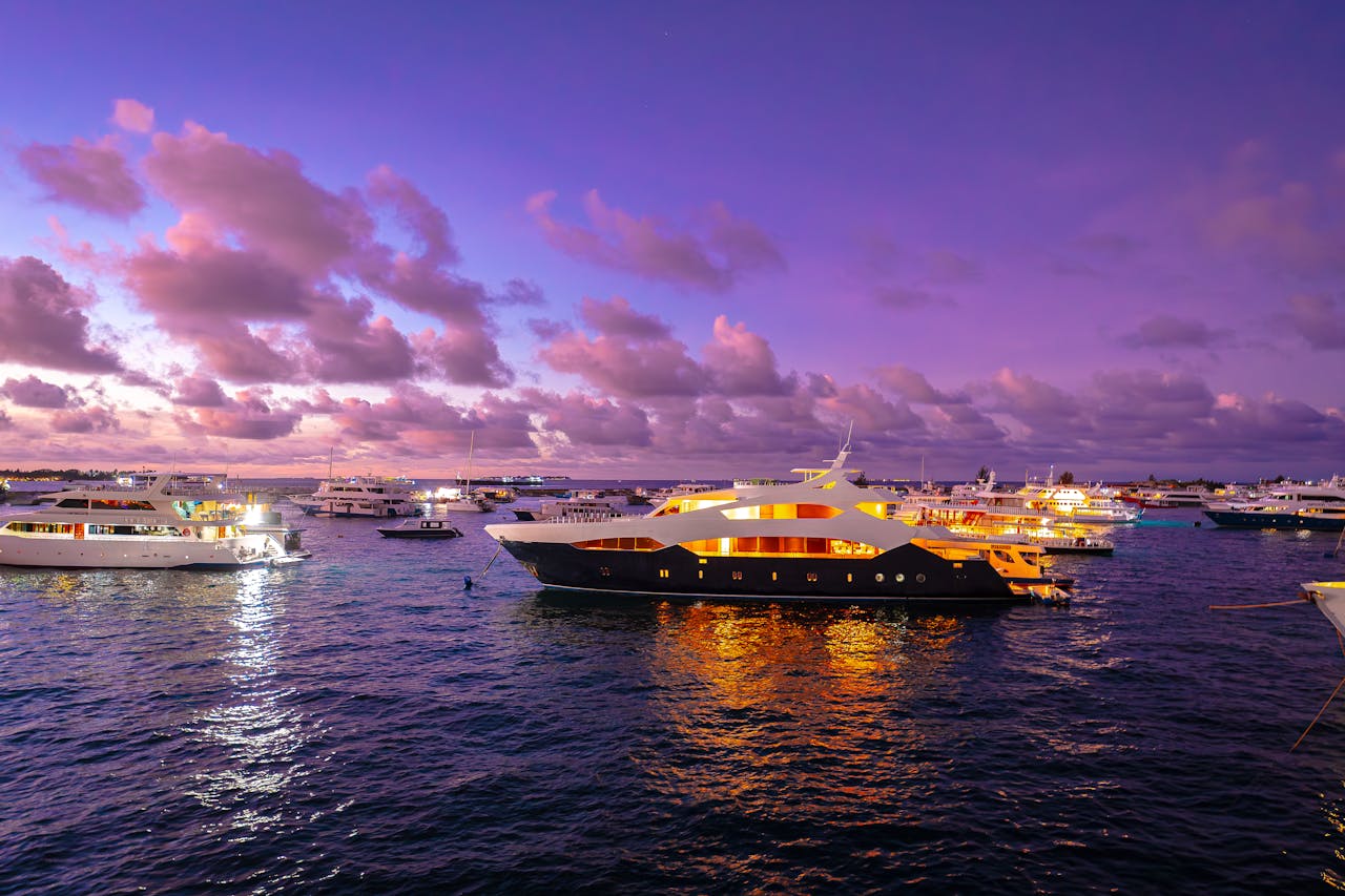Home A scenic view of luxury yachts illuminated at sunset in the Maldives, offering a serene travel experience.