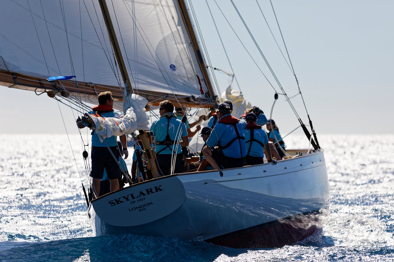 A group sailing on a classic yacht named 'Skylark' over shining blue sea waters under clear skies.